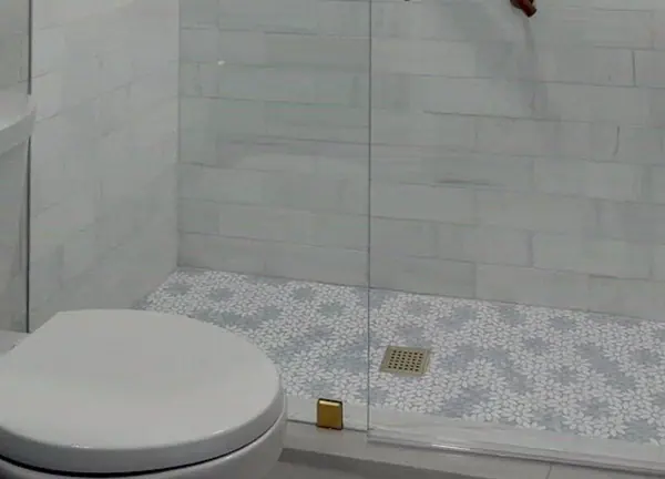 A finished walk-in shower floor with patterned tile and a glass panel