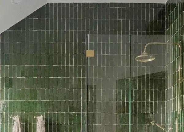 Walk-in shower with green tile and brass fixtures