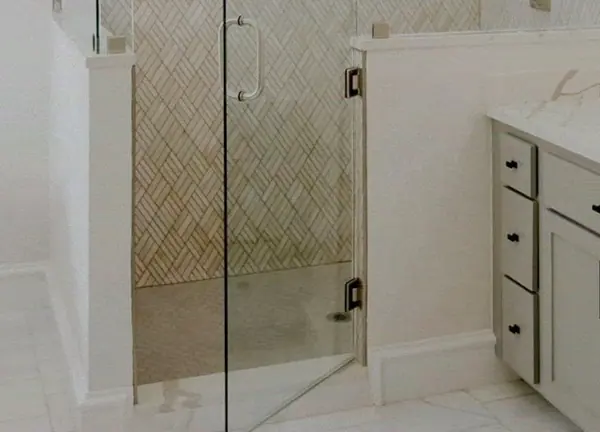 Walk-in shower with a glass door on a half wall and herringbone tile